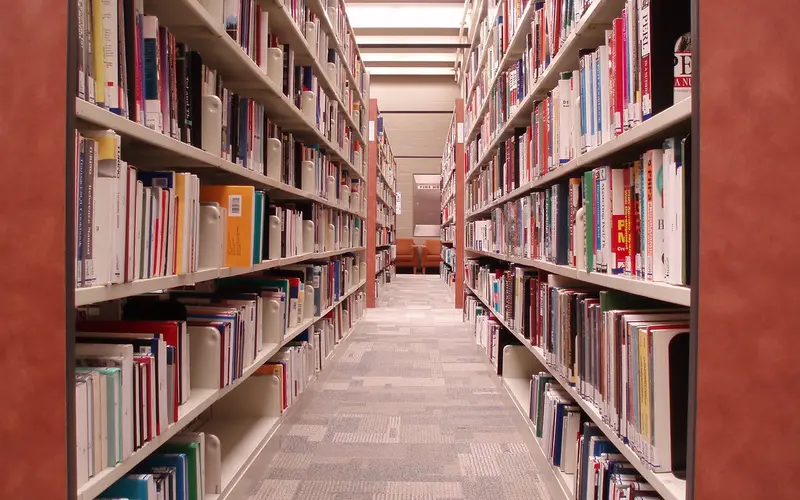 Estantes de biblioteca com livros organizados e mesa de leitura ao fundo