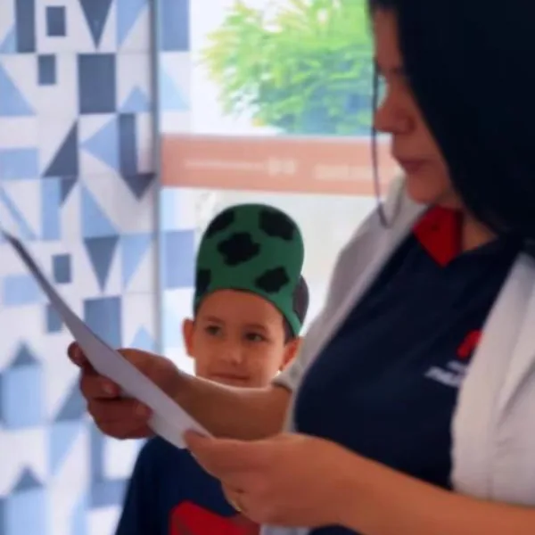 Aluno do 1º ano, de boné, ao lado da professora